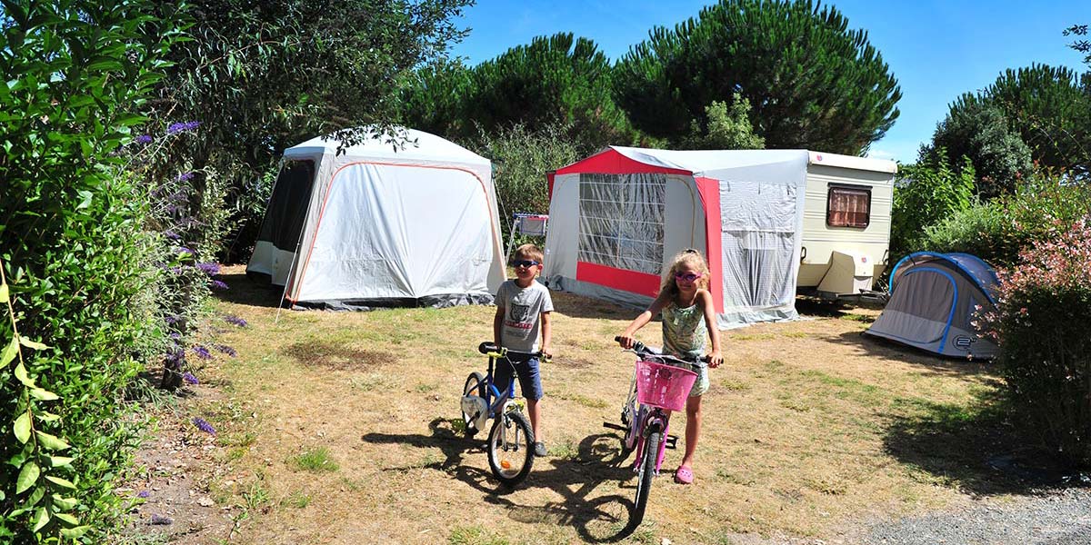 Enfants à vélo devant un emplacement pour tente au camping en Charente Maritime